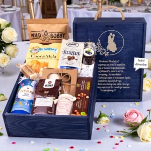 Ekskluzywne podziękowanie dla rodziców w formie eleganckiej granatowej skrzyni z grawerowaną dedykacją ślubną i uchwytem. Bogaty zestaw upominkowy zawiera herbatę Lovare, kawę Sati o smaku piernikowym, włoskie ciastka Mulino Bianco, konfiturę z malin z rumem, praliny oraz owoce w czekoladzie. Prestiżowy upominek ślubny zaprezentowany na tle eleganckiej sali bankietowej z białymi różami, idealny jako wyraz wdzięczności w tym wyjątkowym dniu.