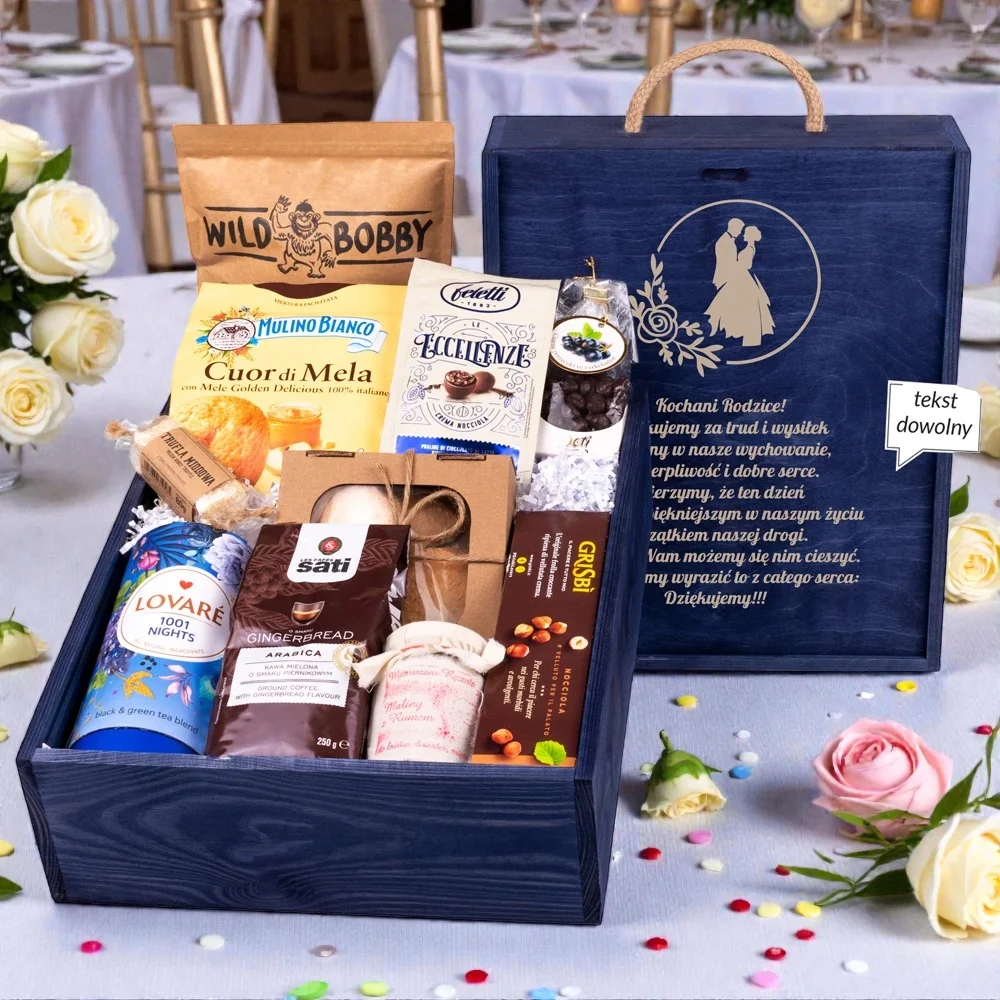 Ekskluzywne podziękowanie dla rodziców w formie eleganckiej granatowej skrzyni z grawerowaną dedykacją ślubną i uchwytem. Bogaty zestaw upominkowy zawiera herbatę Lovare, kawę Sati o smaku piernikowym, włoskie ciastka Mulino Bianco, konfiturę z malin z rumem, praliny oraz owoce w czekoladzie. Prestiżowy upominek ślubny zaprezentowany na tle eleganckiej sali bankietowej z białymi różami, idealny jako wyraz wdzięczności w tym wyjątkowym dniu.